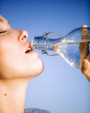 A woman drinking a glass of water, feeling the wellness benefits of proper hydration.