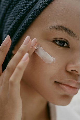 A woman with glowing skin applying moisturizer